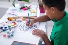 painting-dark-skinned-primary-school-age-boy-drawing-with-blue-pencil-sideways-camera-while-si...jpg